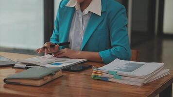 mujer de negocios asiática que usa una computadora portátil y trabaja en la oficina con un documento de calculadora en el escritorio, planificando el análisis del informe financiero, la inversión del plan de negocios, el concepto de análisis financiero. video