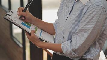 mujer de negocios asiática que usa una computadora portátil y trabaja en la oficina con un documento de calculadora en el escritorio, planificando el análisis del informe financiero, la inversión del plan de negocios, el concepto de análisis financiero. video