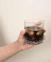 hand is holding a glass of coffee with ices on a white isolated background photo