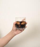 hand is holding a glass of coffee with ices on a white isolated background photo