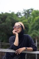 An Asian female model stands confidently on a tennis court, dressed in jeans and a black shirt, adorned with a bandana and glasses photo