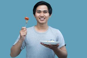 A man in a gray shirt is holding a fork and a plate containing food, for design and visual editing purposes. photo