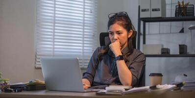 Puzzled confused asian woman thinking hard concerned about online problem solution looking at laptop screen, worried serious asian businesswoman focused on solving difficult work computer task photo