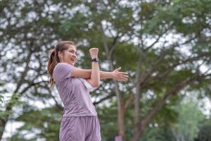 joven asiático mujer toma cuidado de su salud por haciendo ejercicio tramo tu piernas en el parque foto