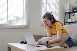 Beautiful Asian woman wearing casual clothes On the sofa using a laptop computer, entertaining with social media, relaxing, smiling and laughing. photo