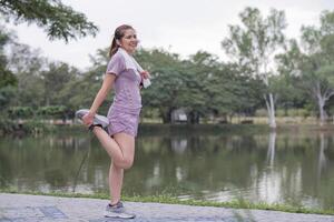 joven asiático mujer toma cuidado de su salud por haciendo ejercicio tramo tu piernas en el parque foto