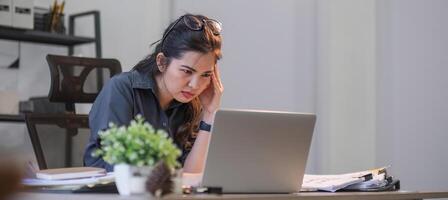 Puzzled confused asian woman thinking hard concerned about online problem solution looking at laptop screen, worried serious asian businesswoman focused on solving difficult work computer task photo