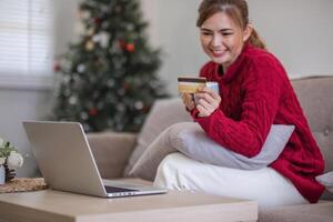 en línea compras. mujer comprando ordenador portátil utilizando crédito tarjeta sentado en sofá a hogar foto