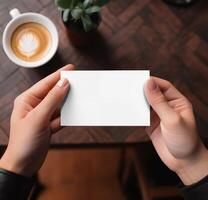 AI generated Hand holding blank white business card mockup on table background with coffee cup photo