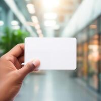 AI generated Close up of hand holding blank white business card mockup on blurred office background photo