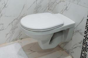 White ceramic toilet hanging on the wall, toilet room, closed toilet cover, plumbing fixed to the wall, restroom. photo