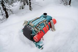 un mochila con cámping engranaje mentiras en el nieve. invierno caminata en el montañas, equipo para escalada. termo con té. foto