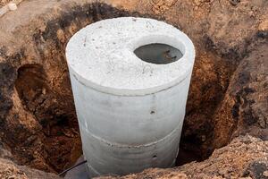 A well made of concrete, a pit for sewerage, a construction site, a connection of communications to the house, the gray color of cement, a round sewer hatch. photo