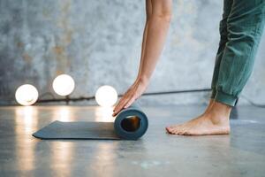 Hands roll the yoga mat on the floor. The girl puts a mat for fitness on the floor of the legs standing next to each other. Close-up of training accessories. A bundle of rubber. photo