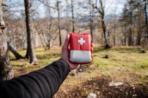 A man's hand holds a first aid kit against the background of the forest, first aid in a hike, a bag with a red cross, emergency first aid to a traveler in trouble, a necessary thing photo