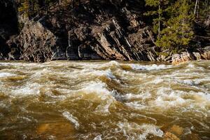 A powerful threshold on a mountain river, the water is bubbling in the channel, the steep rock breaks off into the water, the flow of muddy water, flooding, Aigir Bashkortostan Russia. photo