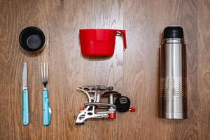 Equipment for tourism a set of dishes, gas burner, thermos, mug, knife, fork. Pack your things for a hike. Leisure items are laid out on the floor view from above. photo