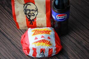 Bangkok, Thailand - March 3, 2024 - KFC Chicken Zinger Burger and Fresh Fries with Pepsi Soda Placed on a black wooden table, takeaway food, junk food, KFC fried chicken, Pepsi New logo. photo