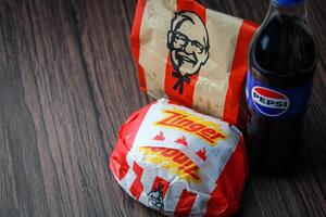 Bangkok, Thailand - March 3, 2024 - KFC Chicken Zinger Burger and Fresh Fries with Pepsi Soda Placed on a black wooden table, takeaway food, junk food, KFC fried chicken, Pepsi New logo. photo