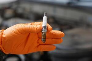 Close up mechanic hands hold old spark plug, spare part of car engine. Concept, machine maintenance, fix, repair, check or diagnose automobile problems by engine specialist. photo