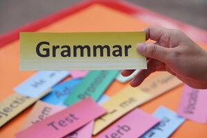 Close up student hands hold paper word card with text Grammar. Concept, English language grammar teaching. Using word card to create for playing educational fun games or practice photo
