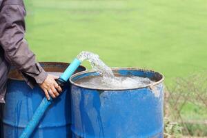 Close up farmer hand hold pipe of water to put into blue buckets in garden. Concept, Solve problems lacking of water in agriculture by prepare water for watering plants in drought season. photo