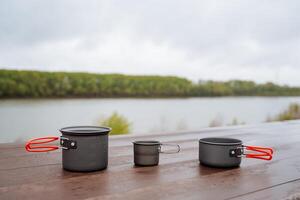 Camping utensils stand on the table, a set of light camping utensils, a pot and two mugs with handles, aluminum alloy pans, food in nature concept photo