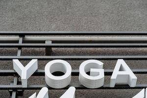 A sign of the word yoga hangs on the wall, white text letters, meditation, fitness room, voluminous printed letters. photo