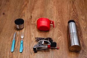 Equipment for tourism a set of dishes, gas burner, thermos, mug, knife, fork. Pack your things for a hike. Leisure items are laid out on the floor view from above. photo