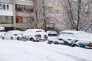 The car is covered with snow. Snowfall in the city. Equipment under the snowdrift. The car got stuck in the snow in the winter. Uncleaned streets of the metropolis. photo