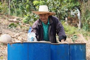 Asian man farmer is working, preparing water into blue buckets in garden. Concept, Solve problems lacking of water in agriculture by prepare water for watering plants in drought season. photo