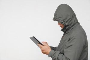 Man hacker wears hoodie, holds smart tablet. Concept, digital information security, Cyber security. Online Criminal. Man is checking and searching information from internet. photo