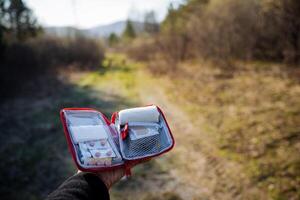 un primeros auxilios equipo con medicamentos en contra el antecedentes de el bosque, un de la persona mano sostiene un bolso con medicamentos, un conjunto de tabletas, un conjunto de vendajes, un paquete de primero ayuda equipo. foto