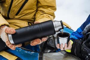 acero termo en mano. verter un caliente bebida dentro un taza. un vaso en su mano con agua. disfrutar en un herbario bebida desde un termo botella. invierno caminata en el bosque. foto