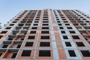 The facade of the house, red brick, many apartments, a tall building, no windows, empty walls, a view from below, a construction site. photo