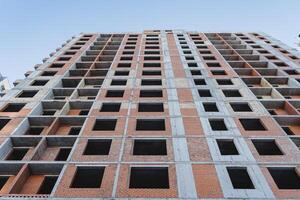 el fachada de el casa, rojo ladrillo, muchos apartamentos, un alto edificio, No ventanas, vacío paredes, un ver desde abajo, un construcción sitio. foto