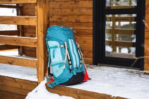 A bright hiking backpack lies on the snow. A climbing rope is tied to a backpack. In the side pocket of the thermos. Hiking in winter. Rocks and forests photo