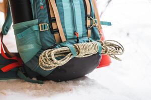 A bright hiking backpack lies on the snow. A climbing rope is tied to a backpack. In the side pocket of the thermos. Hiking in winter. Rocks and forests photo