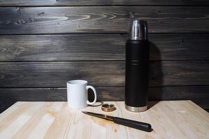 A set of camping utensils. Thermos, cutter,compass and white mug. Camping, eating outdoors. Prepare for travelling. photo