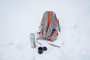 Equipment for hiking in winter. A thermos, a backpack and a glass lie in the snow. A halt on a winter trip. photo