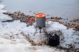 Tourist dishes for cooking, a light aluminum pot for water, equipment for hiking gas burner of their metal, dishes stand on the bank of the river. photo