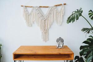 The bright interior of the room is the head of the Buddha standing on the table. Minimalistic design of the workplace in the apartment. Silver Buddha, boho style on the wall. photo