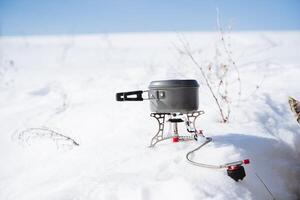 A tourist pot stands on a gas burner in the snow, the cold season, harsh conditions, camping utensils, hiking in winter. photo