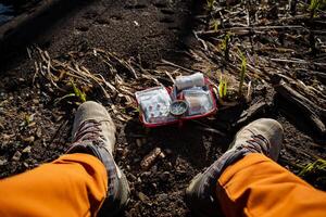 The first aid kit lies on the ground next to the feet of a human tourist, an open bag with medicines, a copper compass, a person got lost in the forest, got lost on the ground. photo