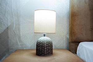 The lamp stands on the bedside table, the night light illuminates the room, bedside reading light, white sconces, ceramic lamp, light bulb design. photo