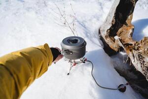 Cooks food on a hike on a gas burner. Camping gas, cooking, hand holding a pot of food, light equipment of a tourist in a winter hike. photo