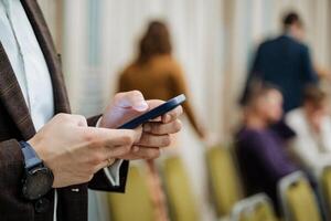 A businessman prints a message on his phone during a conference. A smartphone in the hands of a young guy. Write text with your fingers. Watch on hand. photo