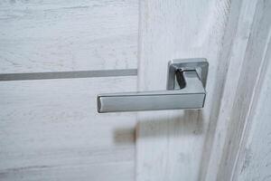 Silver handle at the wooden door. The entrance to the room. The door is made of light wood. Movable element of the door. photo