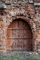 antiguo de madera puerta de rojo color, Entrada a el antiguo estructura, destruido ladrillo, fortaleza fragmento de el puerta, arco en el castillo muro, histórico edificio foto