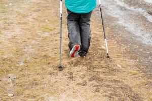 pies en pantalones Vamos a lo largo el camino, nórdico caminando, un turista camina a través de el campo propensión en trekking postes, el único de un zapato, un caminar en el Fresco aire. foto